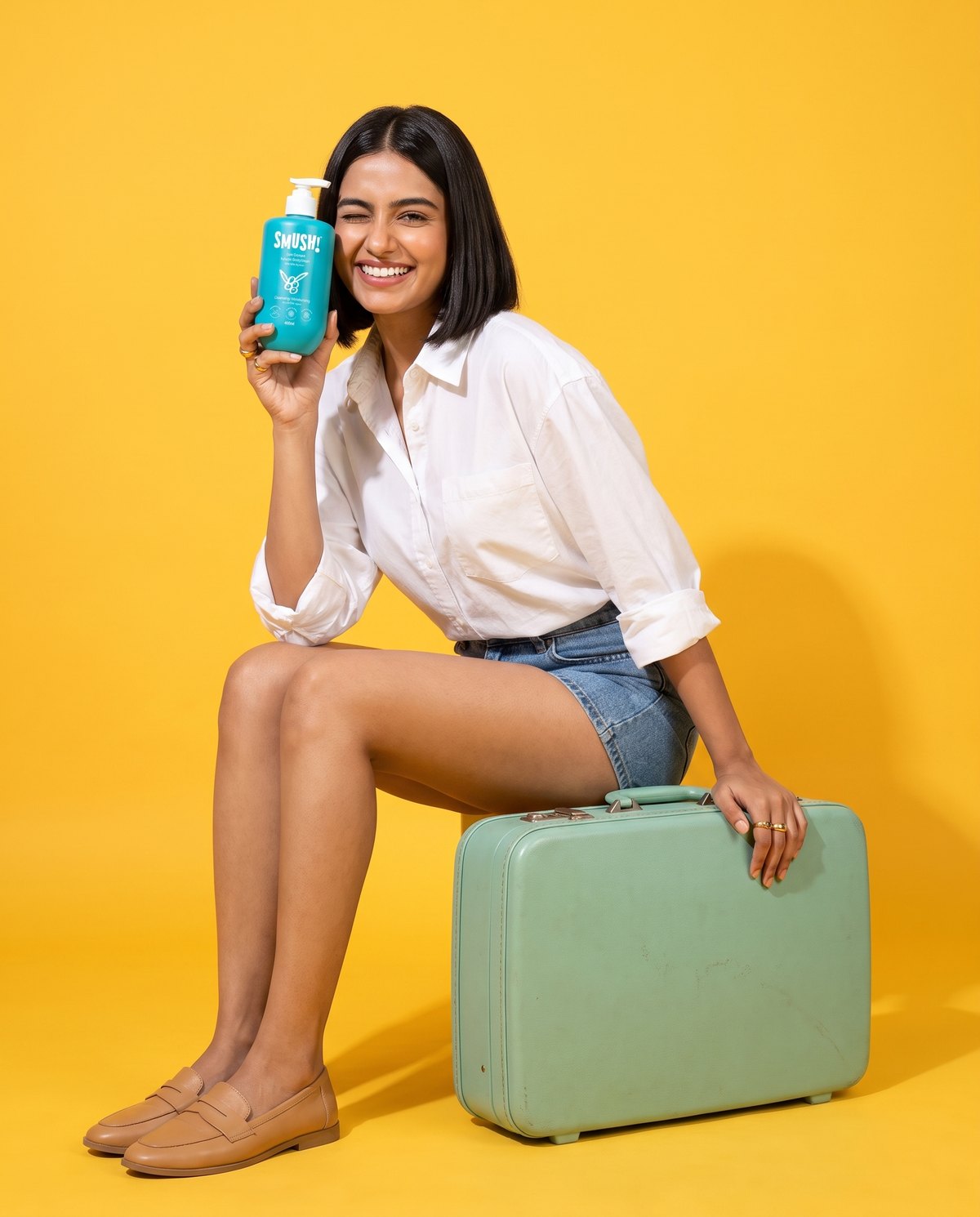 Woman on a mint suitcase holding Ape Escape Kokum Body Wash on a yellow set