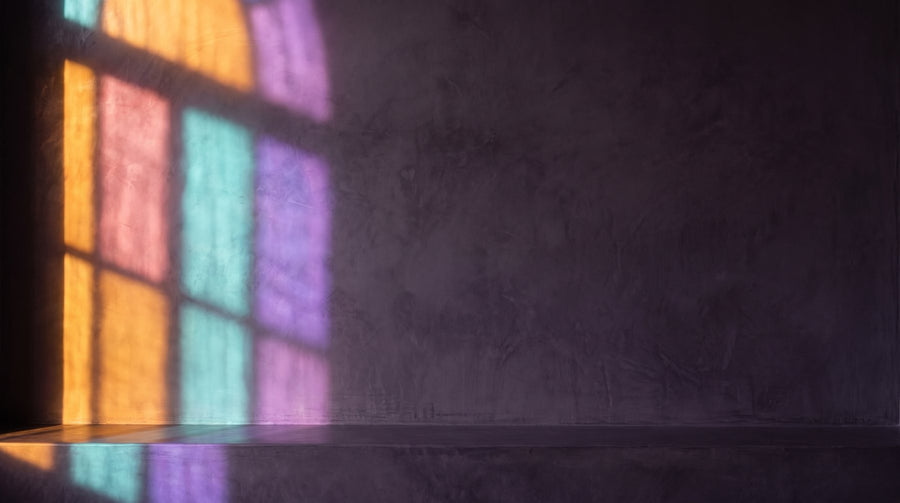 A deep aubergine plaster room at dusk, coloured-glass window light in orange, teal and violet falling on the left wall and ledge