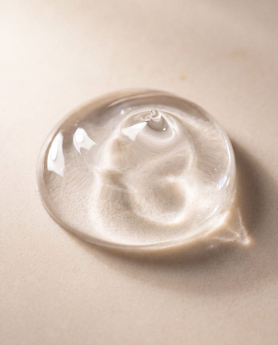 A clear dome of SMUSH! body wash gel on a warm cream surface, light catching its edge