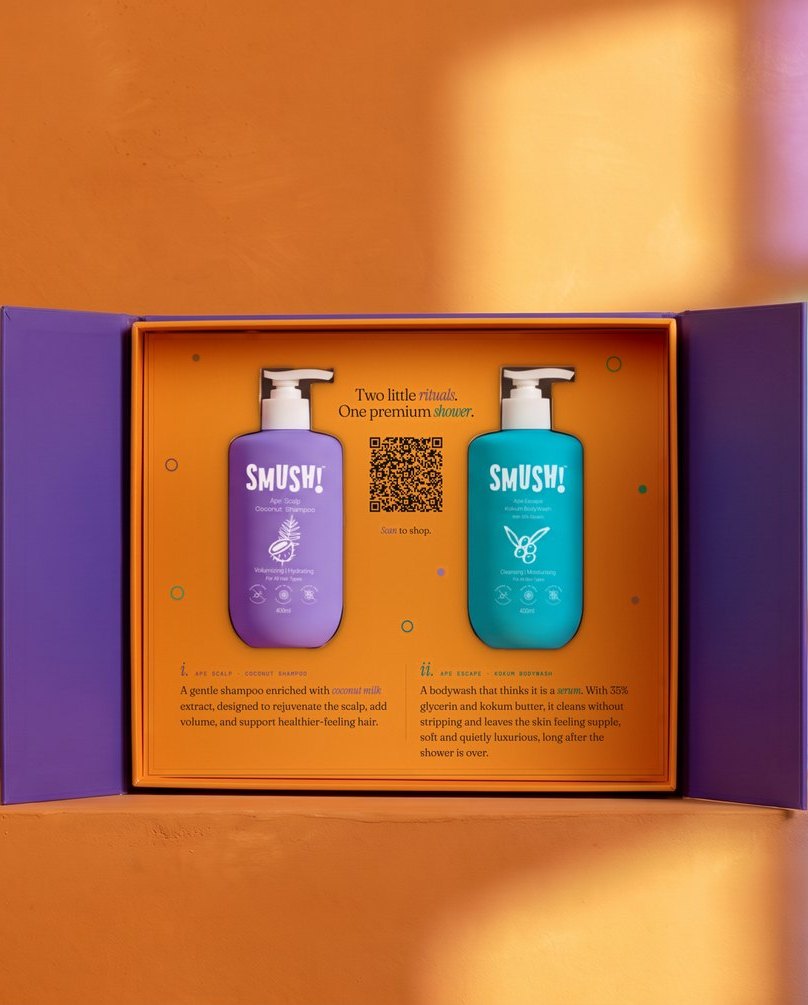The SMUSH! gift box open on a saffron ledge, its purple doors swung out, the shampoo and the body wash standing in the orange tray