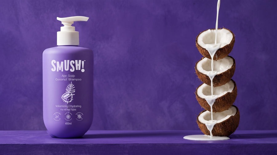 SMUSH! Ape Scalp Coconut Shampoo, a purple pump bottle on a violet limewash ledge, with milk pouring down a tower of halved coconuts beside it